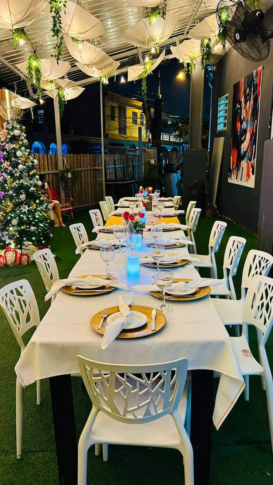 Mesa montada con vajilla dorada bajo el techo de luces, junto a un árbol iluminado.
